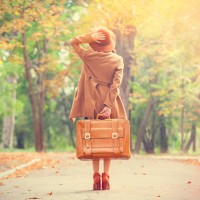 Redhead girl with suitcase in the autumn park.